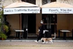 A woman wearing a protective mask walks her dog in Piazza Navona, as Italians remain under lockdown to prevent the spread of the coronavirus disease (COVID-19), in Rome, Italy, April 4, 2020.
