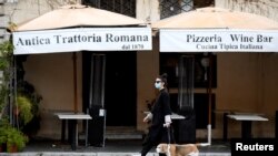 A woman wearing a protective mask walks her dog in Piazza Navona, as Italians remain under lockdown to prevent the spread of the coronavirus disease, in Rome, April 4, 2020.