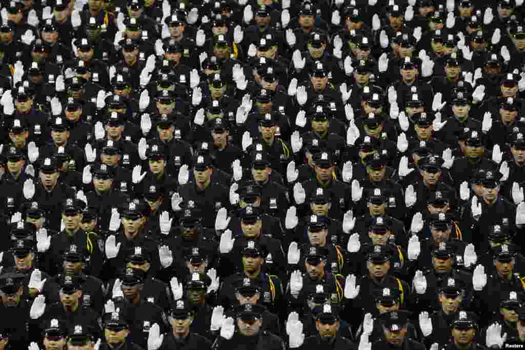 Members of the class of the New York City Police Academy raise hands during their graduation ceremony at Madison Square Garden in New York.