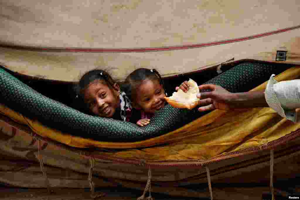 A man offers bread to children as they look out from a tent in front of the Defense Ministry in Khartoum, Sudan.