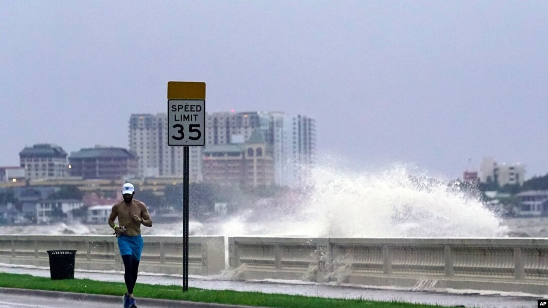 A jogger makes his way along Bayshore Blvd., in Tampa, Fla. as a wave breaks over a seawall, during the aftermath of Tropical Storm Elsa, July 7, 2021.
