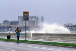 FILE - A jogger makes his way along Bayshore Blvd., in Tampa, Fla. as a wave breaks over a seawall, during the aftermath of Tropical Storm Elsa, July 7, 2021.