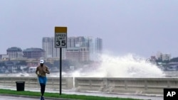 A jogger makes his way along Bayshore Blvd., in Tampa, Fla. as a wave breaks over a seawall, during the aftermath of Tropical Storm Elsa, July 7, 2021. 
