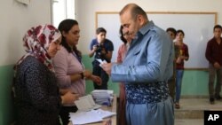 In this picture provided by the Press Office of the Kurdish Self-administration Office in Kobani, a Kurdish man, right, reads a paper before he ballots his vote to elected new local councils of the three Kurdish-administered areas in northern Syria, known as Rojava, at a polling station, in Kobani, Syria, Sept. 22, 2017. 