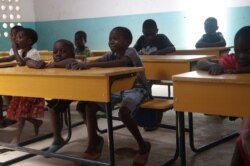 These children at Mazembe Primary School used to sit on the floor before Ripple Africa donated desks for them. (L. Masina/VOA)