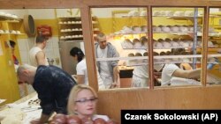 A worker carrying trays of doughnuts 'Paczki' at a pastry shop for Fat Thursday in central Warsaw, Poland, Thursday, Feb. 4, 2016.