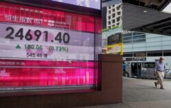 A man wearing a face mask walks past a bank's electronic board showing the Hong Kong share index at Hong Kong Stock Exchange June 23, 2020.