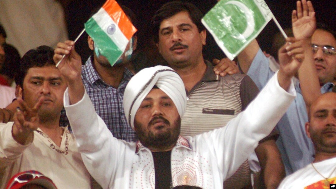 FILE - Indian pop star Daler Mehndi, center, waves Indian and Pakistani flags while watching a cricket match in Lahore, Pakistan, March 24, 2004.