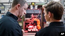 FILE - A.J. Scherman, 37, left, works with fellow apprentice Ryan Buzzy on a robotics control computer at a chainsaw assembly line at a Stihl Inc. production plant in Virginia Beach, Va.. May 25, 2017. 