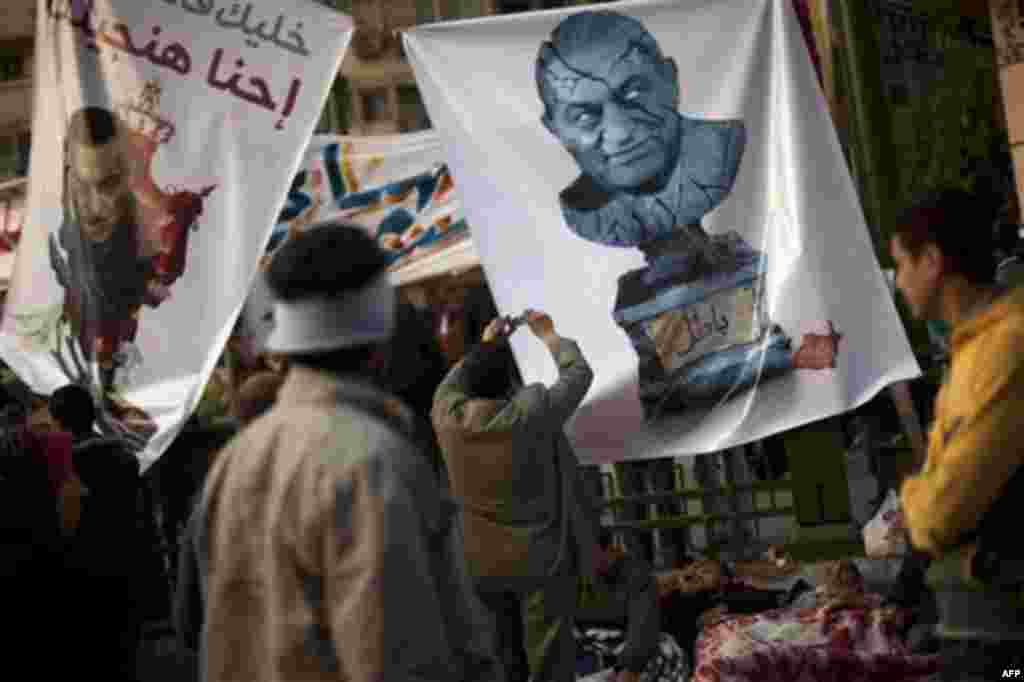 Anti-government protestors stand next to posters with cartoons of President Hosni Mubarak at Tahrir square in Cairo, Egypt, Wednesday, Feb. 9, 2011. Protesters appear to have settled in for a long standoff, turning Tahrir Square into a makeshift village w