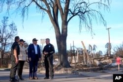 U.S. President Donald Trump and first lady Melania Trump walk with Jason Hing, chief deputy of emergency services at the Los Angles Fire Department, left, and Captain Jeff Brown, chief of Station 69, as they tour a neighborhood affected by wildfires in Los Angeles, Jan. 24, 2025.