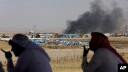 Les habitants du village de Jabir observent les livraisons d'aide aux Syriens qui fuient l'offensive du gouvernement dans le sud alors que la fumée d'un feu inconnu se lève, le 3 juillet 2018.