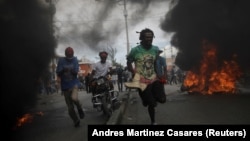 Para pengunjuk rasa berlari melewati ban-ban yang terbakar dalam demo menuntut pengunduran diri Presiden Haiti Jovenel Moise, di Port-au-Prince, Haiti, Rabu, 18 November 2020. (Foto:Andres Martinez Casares/Reuters))