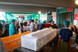 People wearing face masks wait while caskets with bodies are queued outside a crematorium at the Yay Way cemetery in Yangon, Myanmar, July 14, 2021.