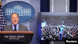川普总统的白宫发言人斯派塞对记者讲话，旁边的电视上显示的是川普就职大典的画面（2017年1月21日）