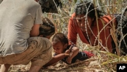 Migrantes que cruzaron a EEUU desde México pasan bajo alambre de púas a las orillas del río Bravo, el jueves 21 de septiembre de 2023, en Eagle Pass, Texas. Fotógrafos de The Associated Press fueron galardonados con el prestigioso Premio Pulitzer de periodismo.