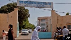 Women walk past the entrance to the University Hospital Fann, where a man is being treated for symptoms of the Ebola virus in Dakar, Senegal, Aug. 29, 2014.