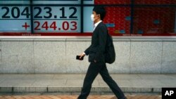 ຊາຍຄົນນຶ່ງໃສ່ຜ້າປິດປາກ ຍ່າງຜ່ານກະດານຂ່າວ ກ່ຽວກັບ ດັດຊະນີຮຸ້ນ Nikkei 225 ຂອງຍີ່ປຸ່ນ ຢູ່ບໍລິສັດຂາຍຮຸ້ນ ໃນນະຄອນໂຕກຽວ (ວັນທີ 11 ພຶດສະພາ, 2020)