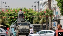 Tunisians walk past a military armored personnel carrier at Habib Bourguiba avenue in Tunis, Tunisia, July 30, 2021. 