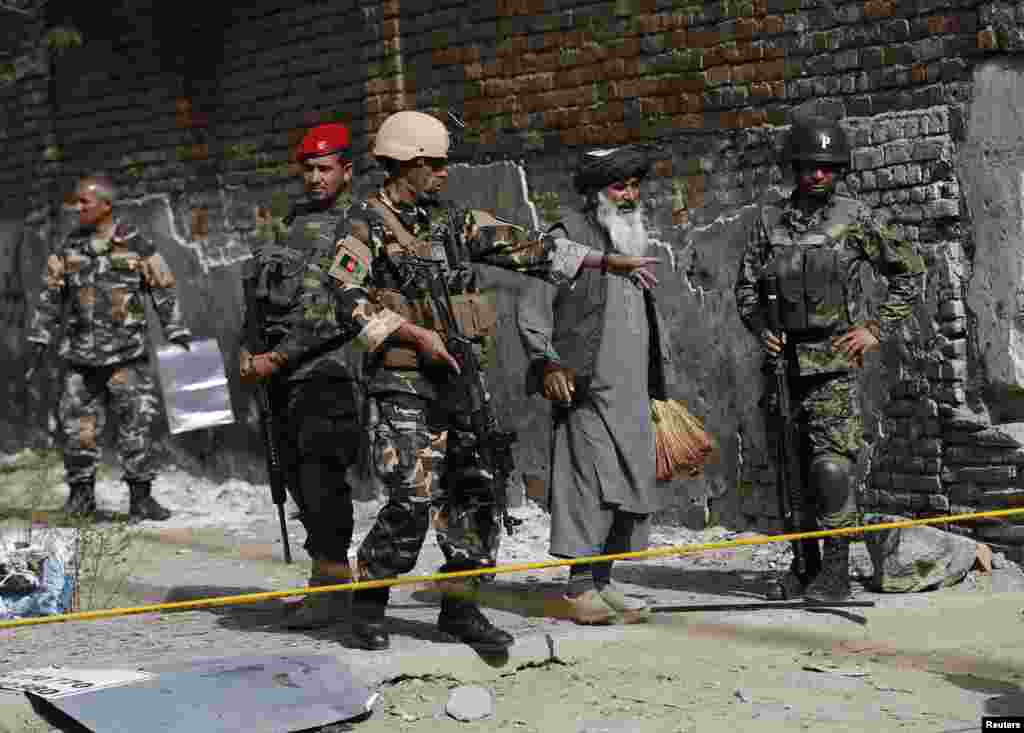 An Afghan security personnel guides a man at the site of a suicide attack in Kabul, July 2, 2014.