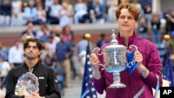 Jannik Sinner, of Italy, holds the championship trophy as Taylor Fritz, of the United States, looks on after Sinner won the men's singles final of the U.S. Open tennis championships, in New York, Sept. 8, 2024. 