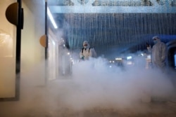 FILE - Volunteers in protective suits disinfect a shopping complex in Wuhan, Hubei province, the epicenter of China's coronavirus disease outbreak, March 31, 2020.