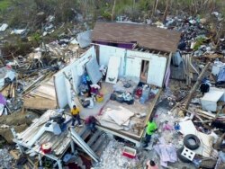 FILE - Two Haitian migrants sit as one stands amid the ruins of a home destroyed by Hurricane Dorian in Abaco, Bahamas, Sept. 28, 2019.