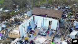 Two Haitian migrants sit as one stands amid the ruins of a home destroyed by Hurricane Dorian in Abaco, Bahamas, Sept. 28, 2019. 