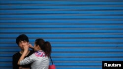 Seorang perempuan sedang membantu pacarnya memencet jerawat di sebuah jalan di Shanghai, 24 April 2012.