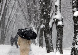 Personas caminan por una calle cubierta de nieve bajo una nevada en Belgrado, Serbia, el domingo 17 de enero de 2021.