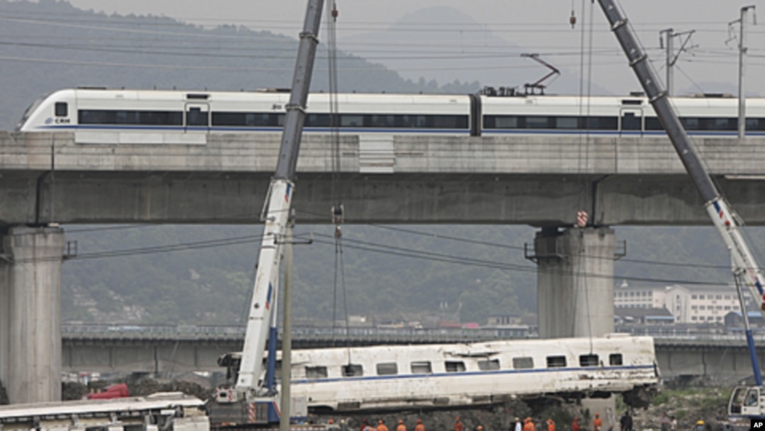 A high speed bullet train runs past a railway bridge as workers use cranes to lift a wrecked carriage onto a truck after two trains crashed and derailed in Wenzhou, Zhejiang province, July 26, 2011.