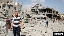 FILE - A Palestinian man carries a gas canister that he salvaged from his destroyed house in Beit Hanoun town, which witnesses said was heavily hit by Israeli shelling and air strikes during the Israeli offensive, in the northern Gaza Strip, July 26, 2014. 