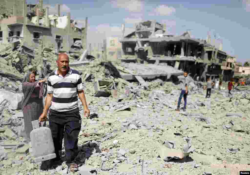 A Palestinian man carries a gas canister that he salvaged from his destroyed house in Beit Hanoun town, which witnesses said was heavily hit by Israeli shelling and air strikes during the Israeli offensive, in the northern Gaza Strip, July 26, 2014. 