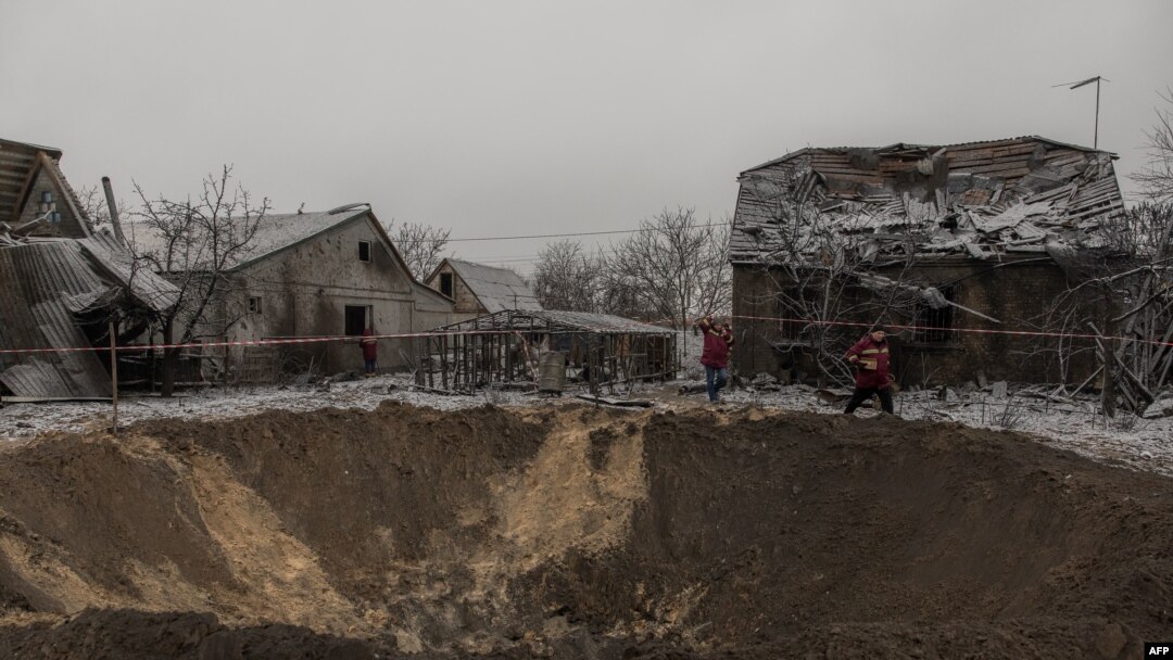 Pekerja komunal berjalan di samping kawah dan rumah-rumah yang hancur akibat serangan Rusia di Kyiv, 11 Desember 2023. (Roman PILIPEY / AFP)