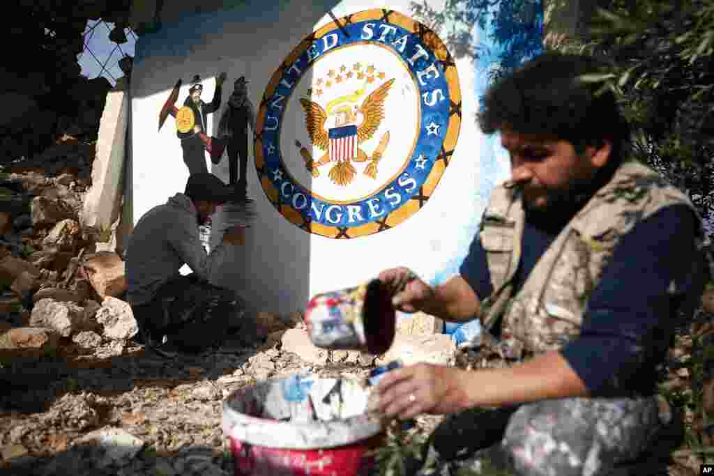 Syrian graffiti artist Aziz Al-Asmar, front, finishes work on his depiction of the events in Washington after U.S. President Donald Trump&#39;s supporters stormed the Capitol, on a wall of a house destroyed in an airstrike, in Binish, Idlib province, Syria.