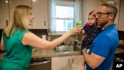 In this Aug. 1, 2018 photo, Lauren Woehr hands her 16-month-old daughter Caroline, held by her husband Dan McDowell, a cup filled with bottled water at their home in Horsham, Pa. 