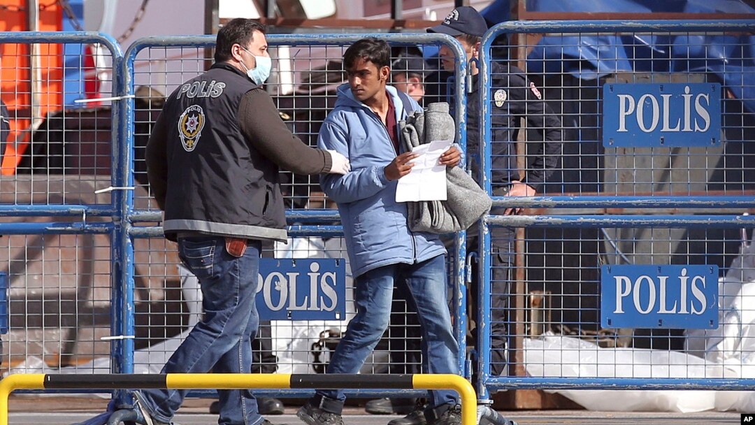 FILE-A masked Turkish police officer escorts a migrant after the first vessel transporting migrants from Greek island of Lesbos was docked in Dikili port, Turkey, putting into practice a European Union plan to stem migration to Europe, April 4, 2016.