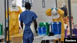 FILE - A Doctors Without Borders health worker takes off his protective gear under the surveillance of a colleague at a treatment facility for Ebola victims in Monrovia, Sept. 29, 2014. 