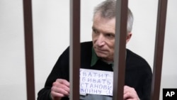 Imprisoned Kremlin critic Alexei Gorinov stands in a cage at the court holding a banner saying "Stop killing, stop the war" in Russian, at his second trial for criticizing Russia's actions in Ukraine, in Vladimir, Russia, Nov. 29, 2024. 