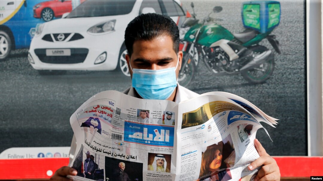 A man wearing a face mask reads a newspaper with the front page headline reporting on Joe Biden's projected U.S. presidential election victory, in Manama, Bahrain, Nov. 8, 2020.