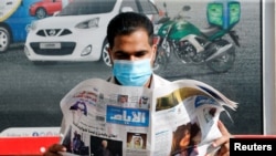 A man wearing a face mask reads a newspaper with the front page headline reporting on Joe Biden's projected U.S. presidential election victory, in Manama, Bahrain, Nov. 8, 2020.