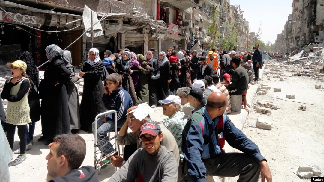 FILE - Residents wait to receive food aid distributed by the U.N. refugee agency at the Palestinian refugee camp of Yarmouk, south of Damascus, Syria, May 2014.