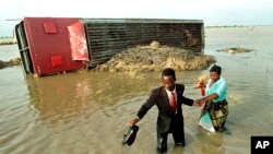 FILE - An unidentified man helps his wife across a river near Xai-Xai, 110 kilometers north from the Mozambique capital Maputo , Tuesday Feb. 22, 2000. In background is a bus that was swept away when the bridge collapsed.