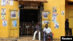 Des hommes assis devant des affiches électorales à Beni, dans la province du Nord-Kivu en RDC, le 5 décembre 2018.