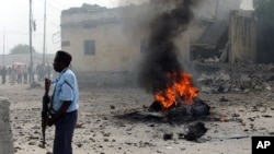 A Somali government policeman stands by a still burning car shortly after it exploded in Somalia's capital, Mogadishu, December 6, 2011.