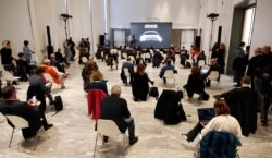 People sit a recommended distance apart from each other during a presentation of the new FIAT 500 electric car, in Milan, Italy, March 4, 2020.