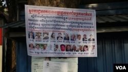 FILE - A poster displays photos of the 18 senior CNRP leaders wanted for arrest in Poipet, Banteay Meanchey province, Cambodia, on November 7, 2019. (Sun Narin/VOA Khmer)