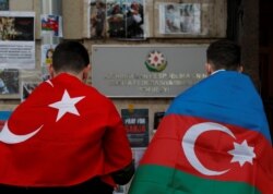 FILE - Men holding national flags of Azerbaijan and Turkey stand next to a memorial for people killed in Azerbaijan during the conflict over the breakaway region of Nagorno-Karabakh, outside the embassy of Azerbaijan in Moscow, Oct. 19, 2020.