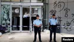 香港警察2019年7月2日站在立法会外被抗议者前一晚示威时涂写在外墙上的涂鸦前。