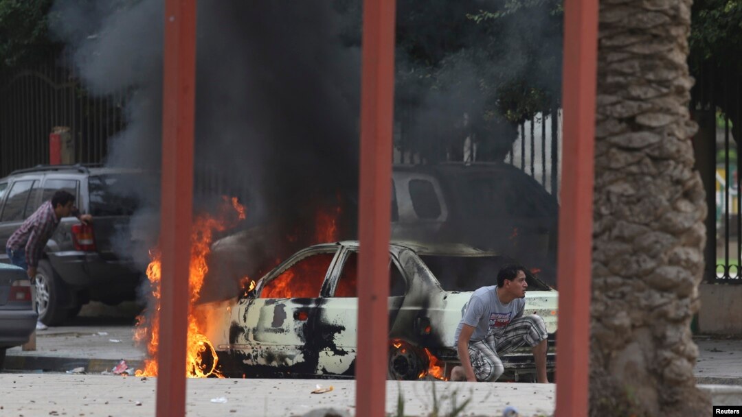Warga di Benghazi berlindung di dekat mobil yang terbakar saat terjadi bentrokan hebat antara tentara Libya dan anggota kelompok Islamis Ansar al-Sharia di Benghazi, Libya, Senin (25/11). 